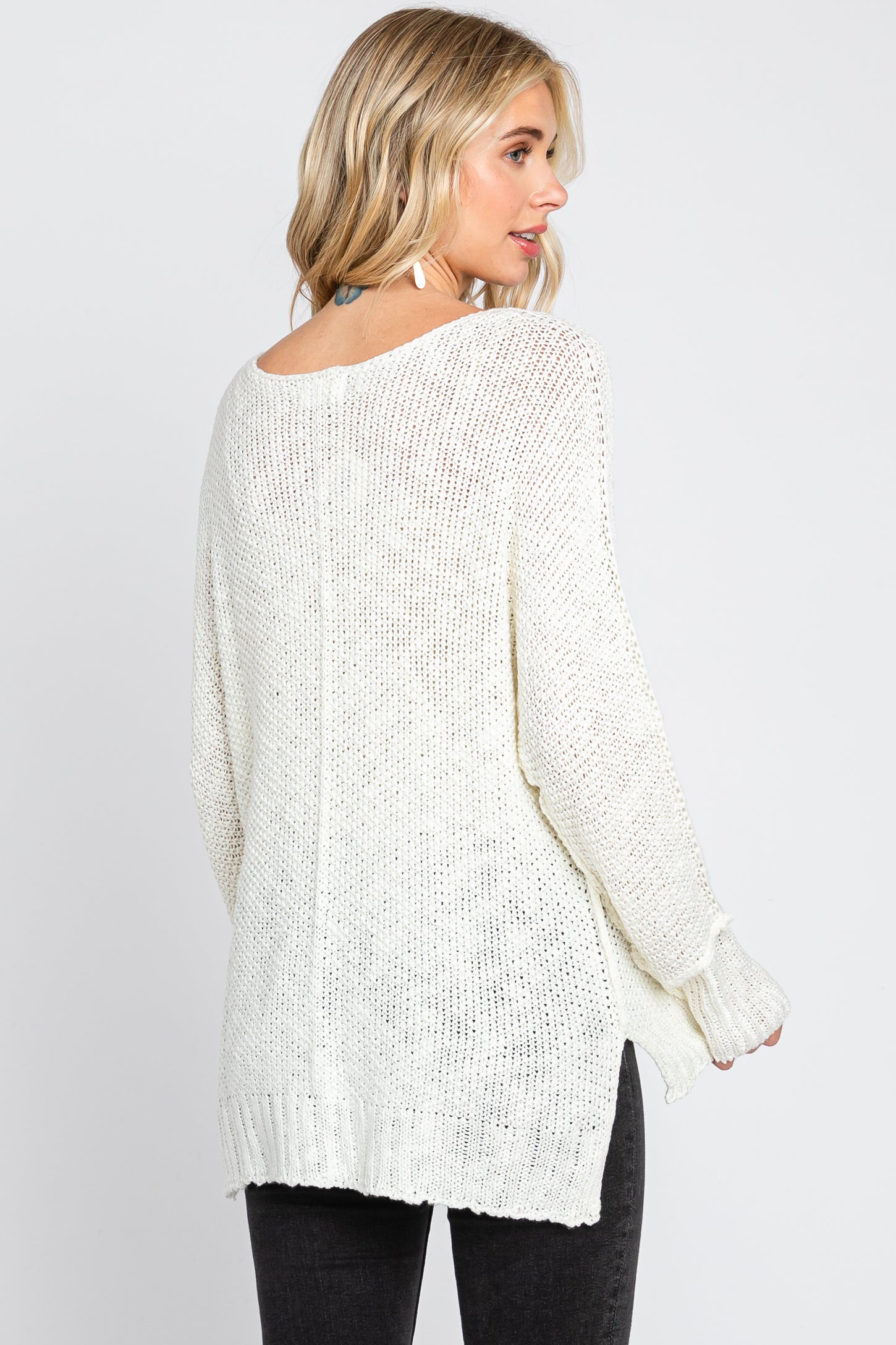 Woman wearing a white oversized knit sweater with side slits and long sleeves, back view