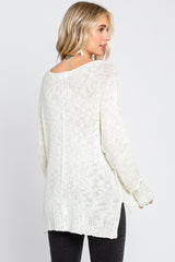 Woman wearing a white oversized knit sweater with side slits and long sleeves, back view