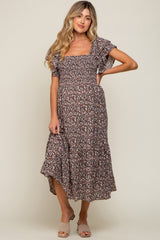 woman wearing a floral print maternity dress with short flutter sleeves and a tiered hemline, standing in a relaxed pose