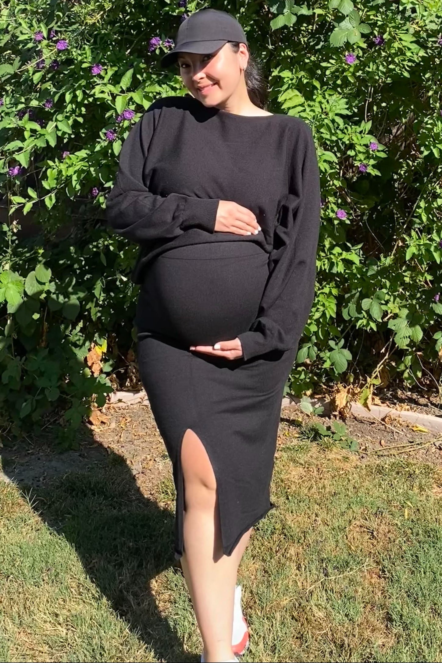woman wearing a black long sleeve maternity dress with a side slit and holding her baby bump
