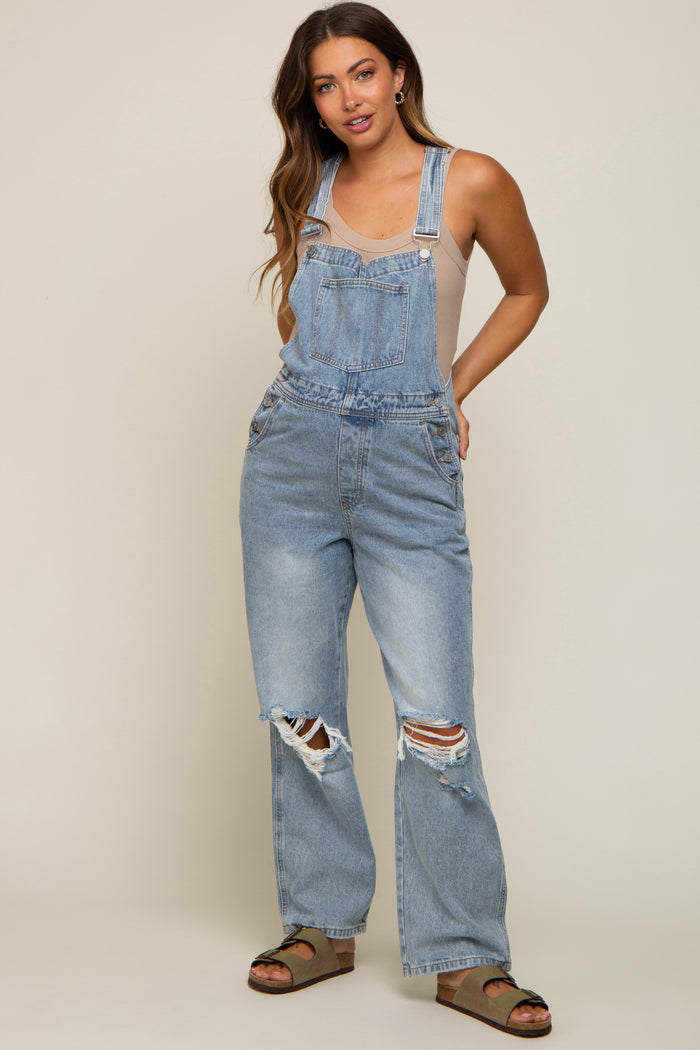 woman wearing a light wash maternity oversized denim overalls with distressed details and a fitted tank top underneath