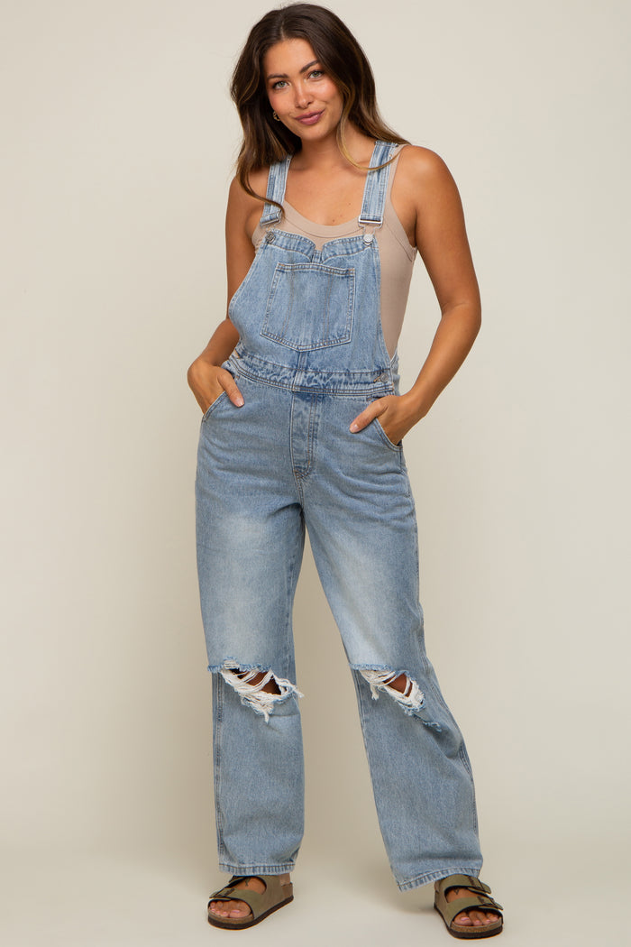 woman wearing light blue distressed maternity overalls with a beige tank top, styled comfortably with pockets