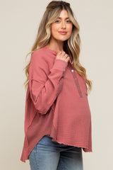 woman wearing a dusty rose maternity top with buttons and raw hem, gently cradling her baby bump
