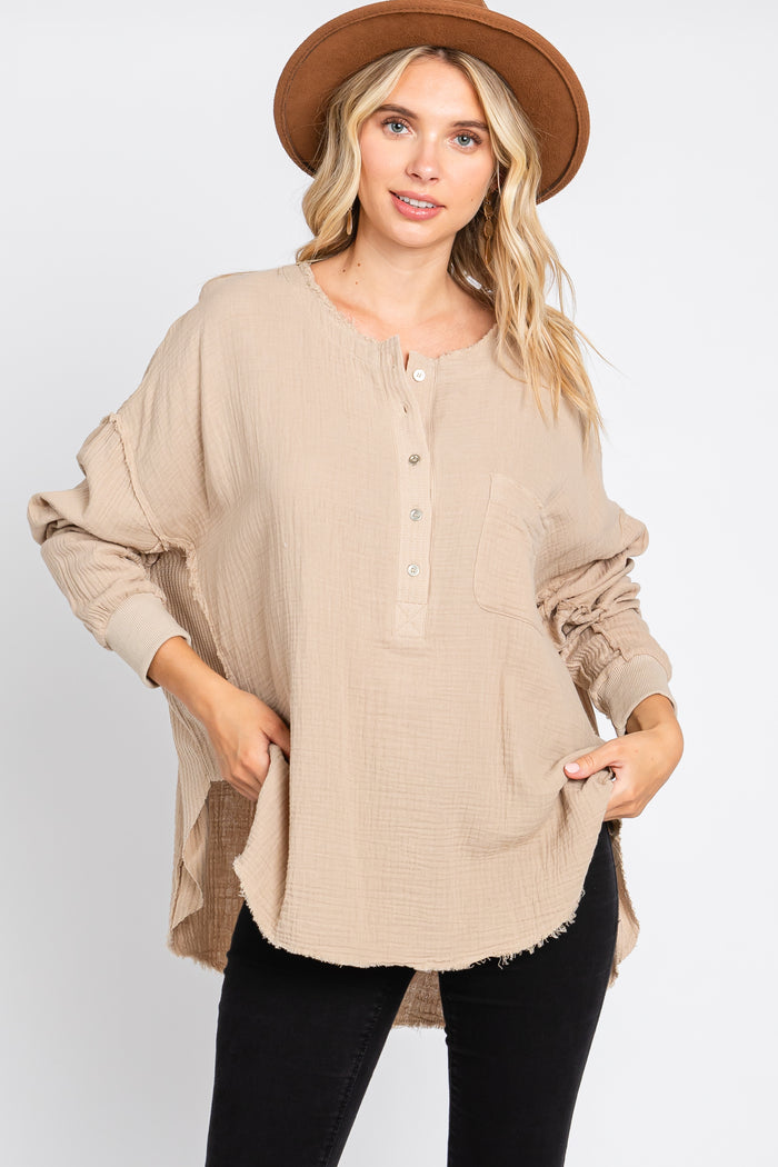 woman wearing a tan long sleeve gauze henley top with a brown wide brim hat and black jeans