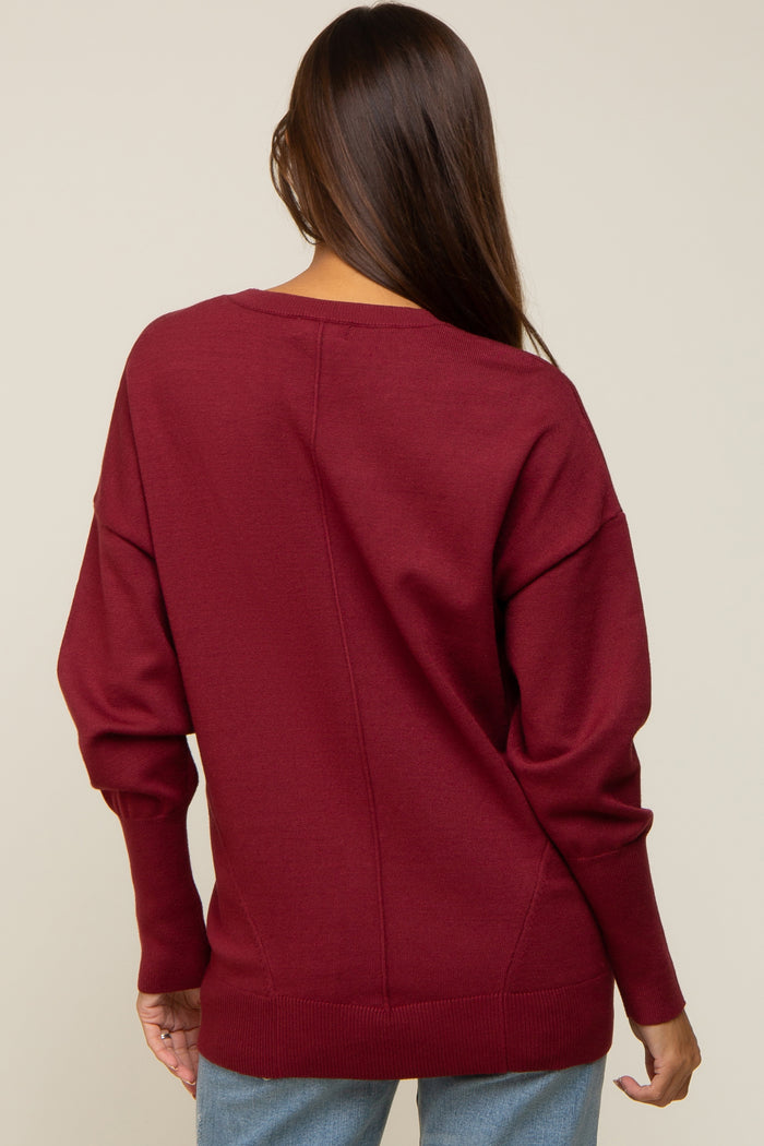 Back view of a woman wearing a burgundy long sleeve knit sweater with seam detail and ribbed cuffs