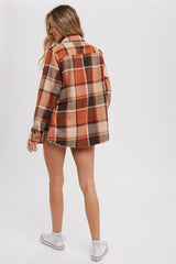 woman wearing an orange and brown plaid oversized flannel shirt, seen from the back, paired with denim shorts and white sneakers