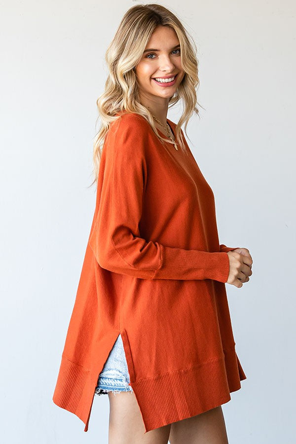 woman wearing an orange oversized sweater with side slits and relaxed fit, paired with denim shorts