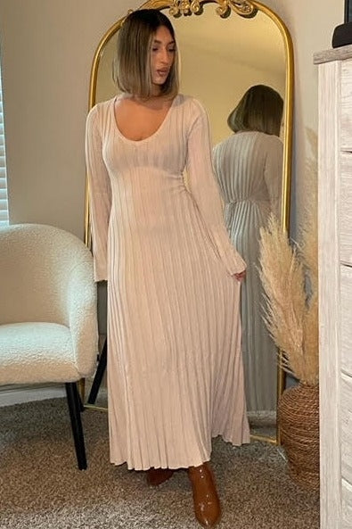 woman wearing a long beige ribbed maxi dress with a v-neck and long sleeves, standing in front of a mirror