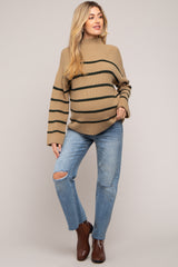 woman wearing a beige and green striped maternity sweater and distressed jeans, showing her baby bump