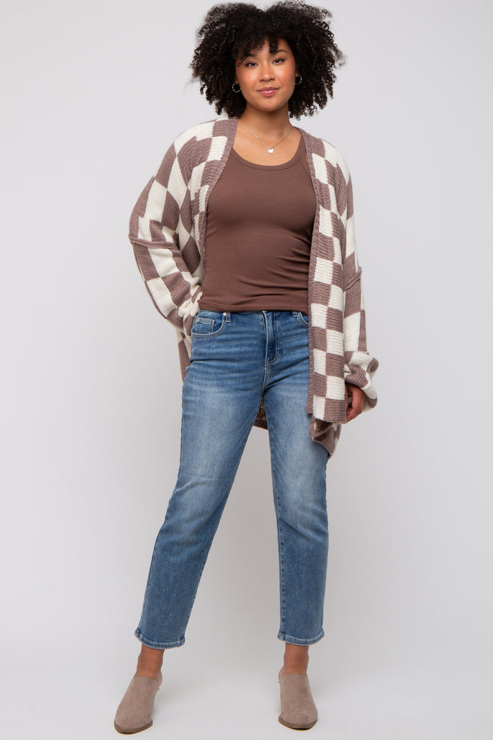 woman wearing a brown and white checkered cardigan over a brown tank top and blue jeans, styled with beige mules