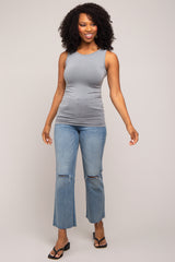 woman wearing a gray sleeveless top and light blue ripped jeans, standing and smiling