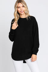 woman wearing a black oversized knit sweater with long sleeves and a ribbed hem, paired with white jeans
