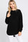 woman wearing a black oversized knit sweater with long sleeves and a ribbed hem, paired with white jeans