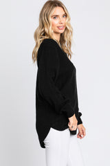 woman wearing a black oversized sweater with textured fabric and side slits, paired with white jeans