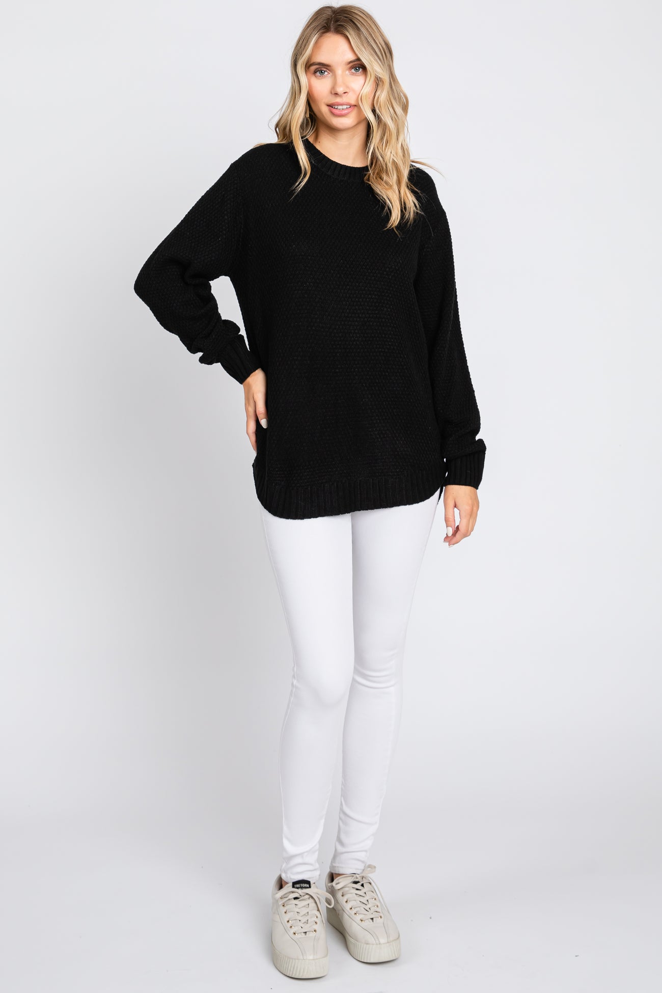 woman wearing a black oversized sweater with long sleeves and white skinny jeans, smiling at the camera