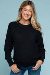 woman wearing a black knit maternity sweater and smiling, with a visible baby bump