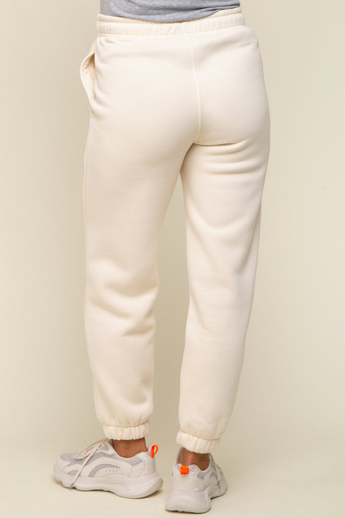 woman wearing cream maternity sweatpants with elastic cuffs and pockets, showing the back view