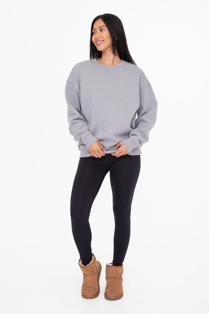 woman wearing a gray oversized sweatshirt, black leggings, and brown ankle boots, standing and smiling