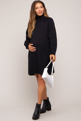 woman wearing a black knit maternity sweater dress and holding her baby bump with a white handbag
