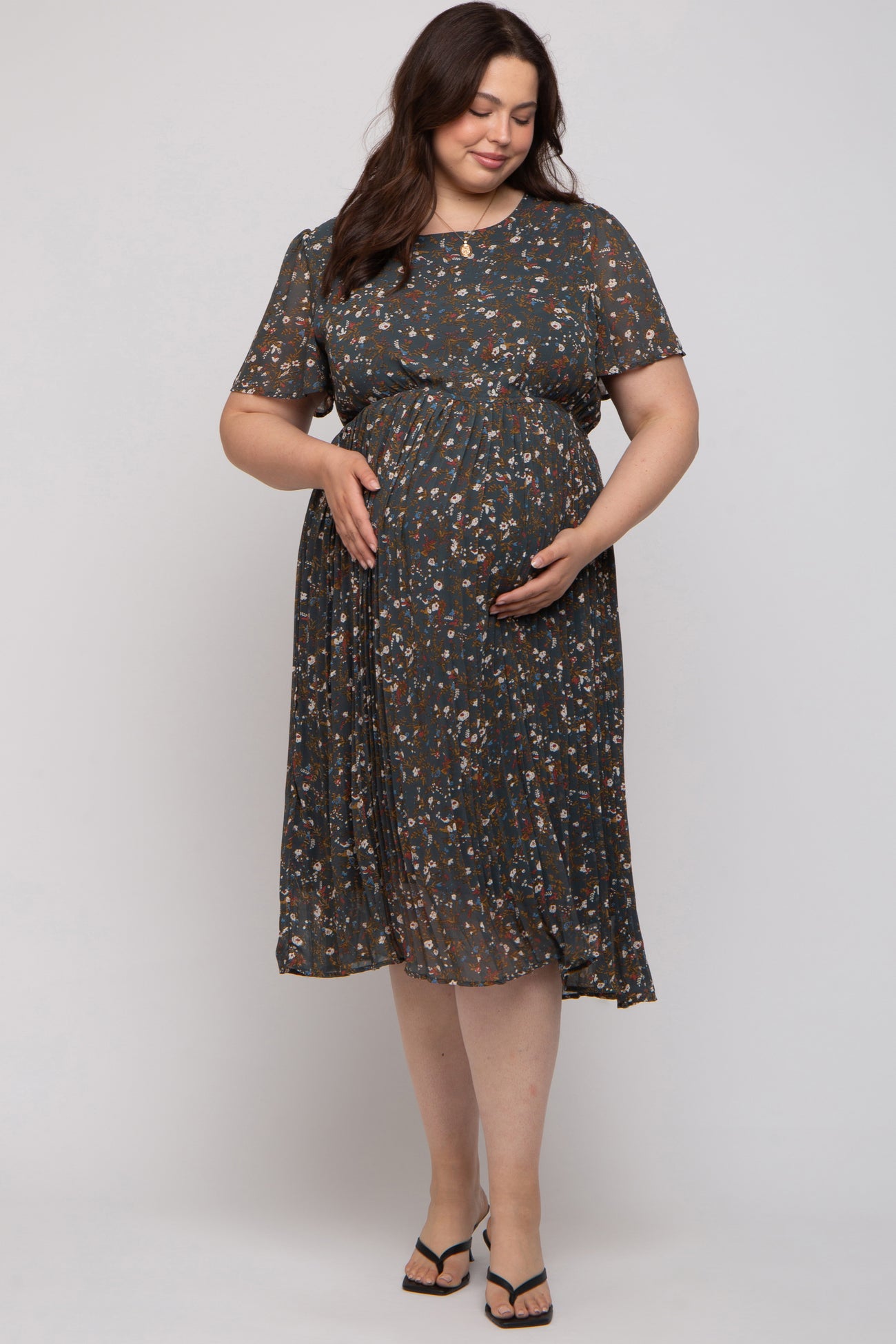 woman wearing a dark floral short sleeve maternity dress and holding her baby bump