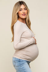 woman wearing a beige long sleeve maternity top and holding her baby bump