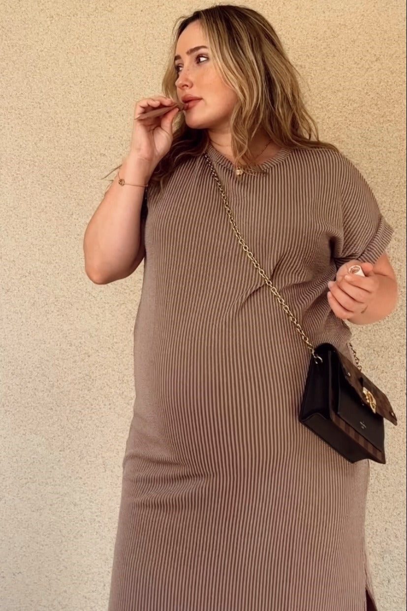 woman wearing a brown striped maternity dress with short sleeves and a baby bump, holding a small handbag