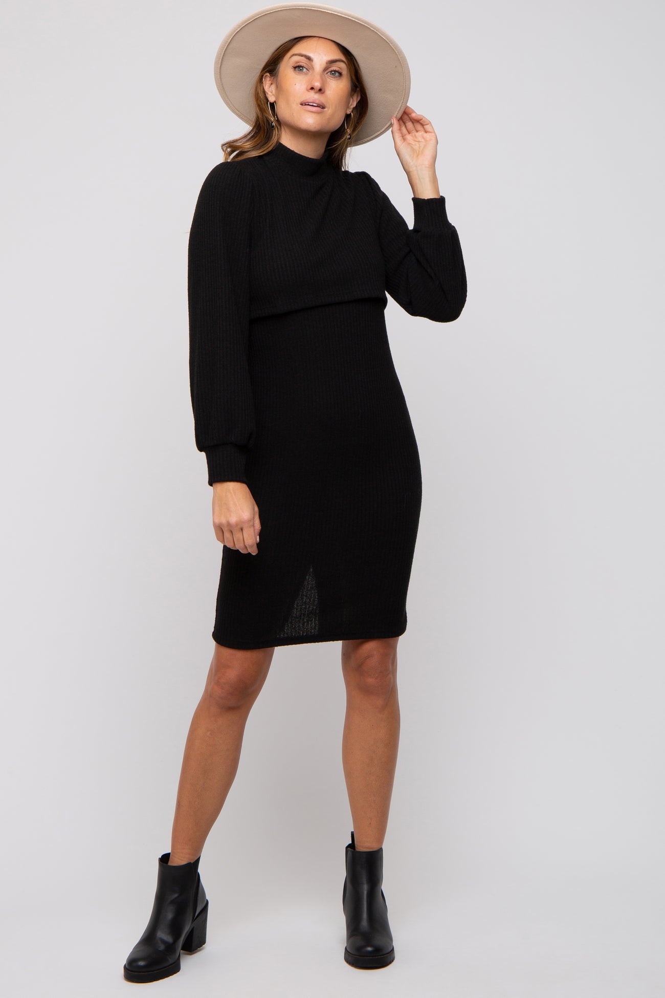 woman wearing a black ribbed long sleeve dress and a wide-brimmed hat, posing with ankle boots on