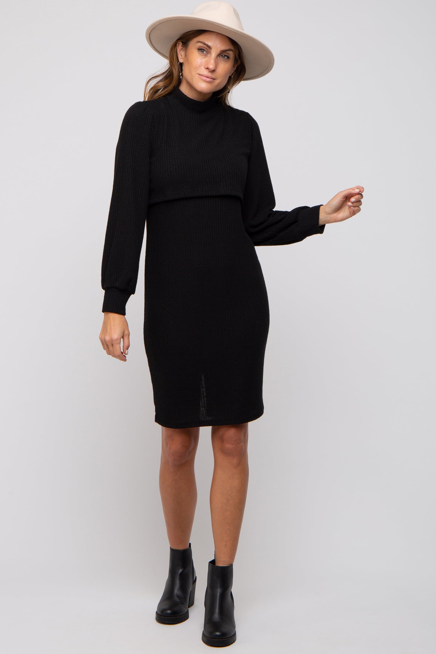 woman wearing a black ribbed long sleeve dress with a high neckline and a front slit, paired with a wide-brim hat