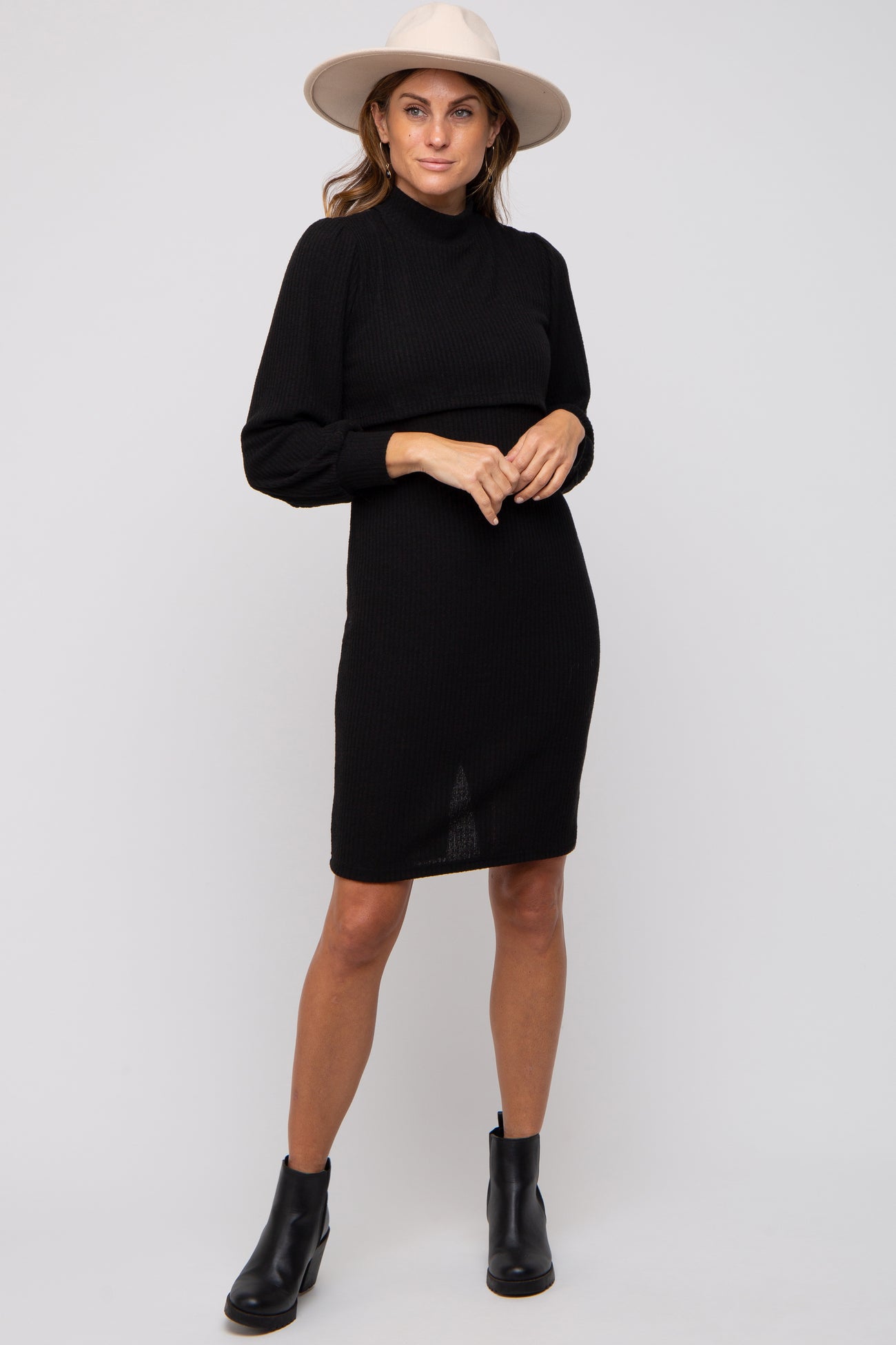 woman wearing a black ribbed long sleeve dress with a high neckline and ankle boots, accessorized with a wide-brimmed hat