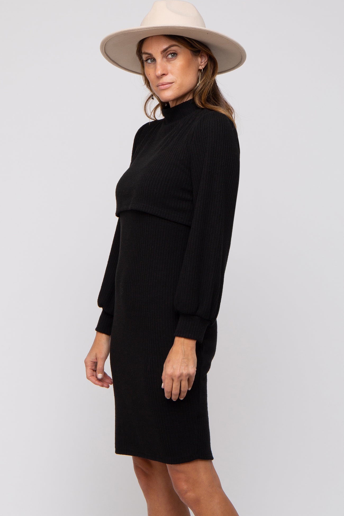 woman wearing a black ribbed knit dress with long sleeves and a mock neck, accessorized with a wide-brim hat