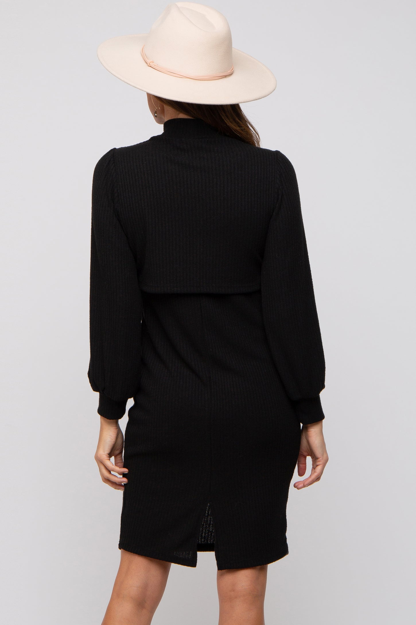 woman wearing a black ribbed long sleeve dress with a high collar and a back slit, styled with a wide-brim hat