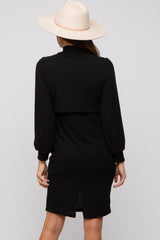 woman wearing a black ribbed long sleeve dress with a high collar and a back slit, styled with a wide-brim hat