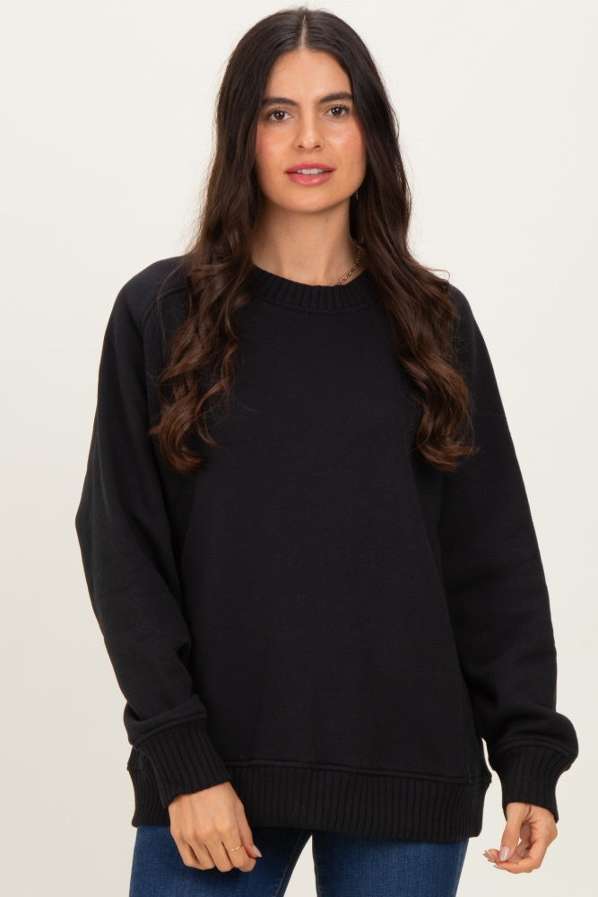 woman wearing a black oversized sweatshirt with ribbed cuffs and hem, posing against a neutral background