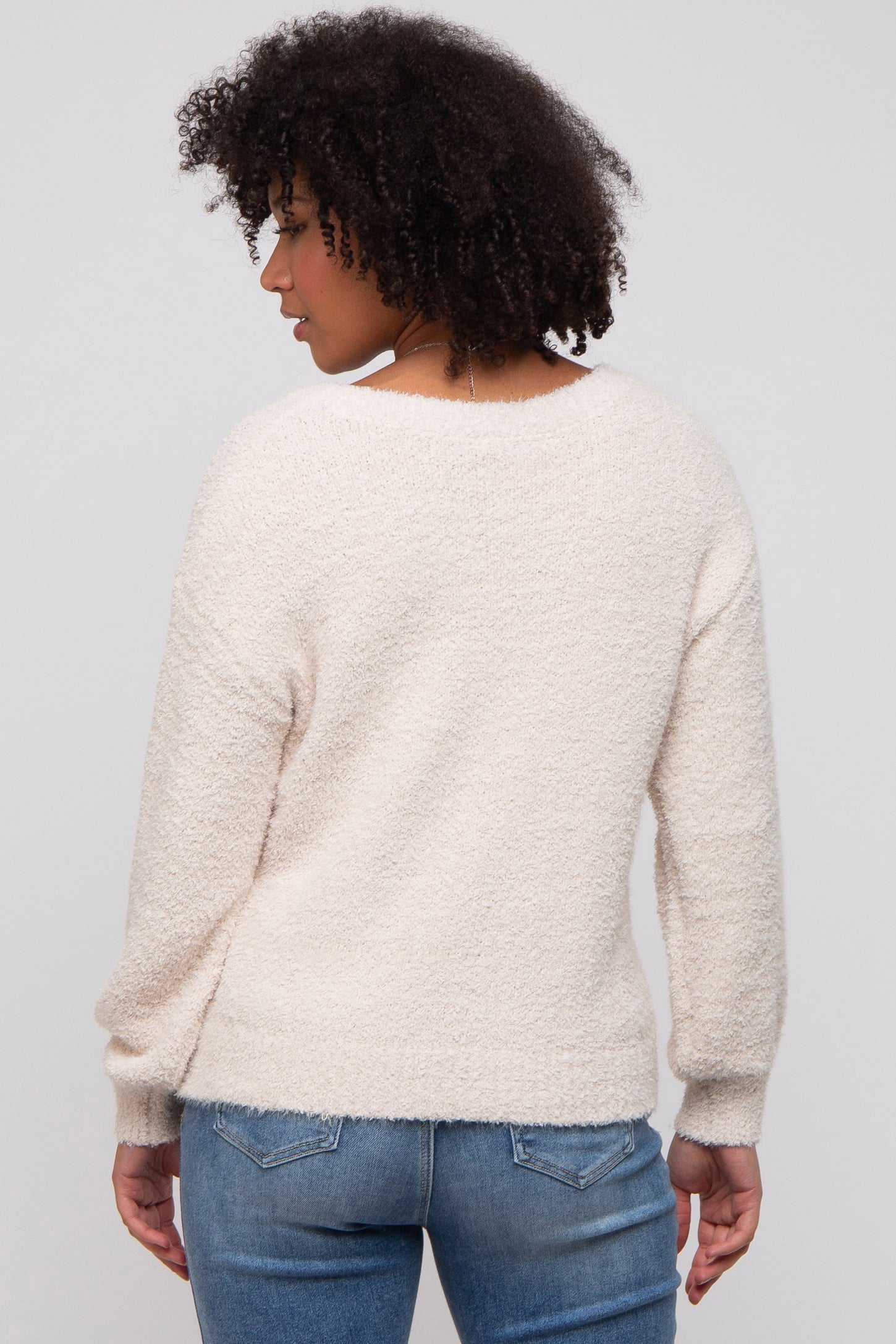 woman wearing a cozy cream-colored textured sweater with long sleeves and a relaxed fit, seen from the back