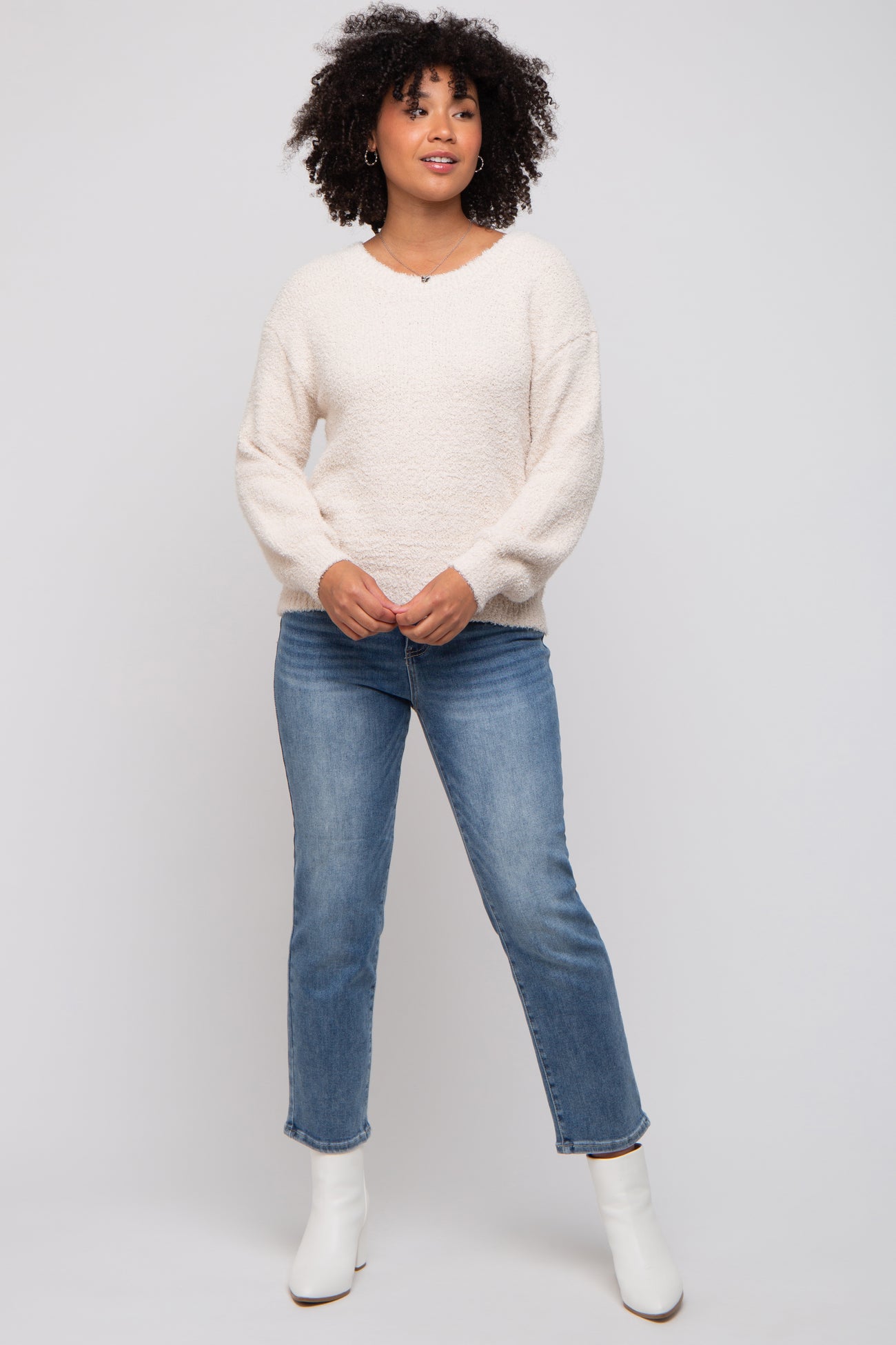 woman wearing a cream fuzzy oversized sweater and blue straight leg jeans with white ankle boots
