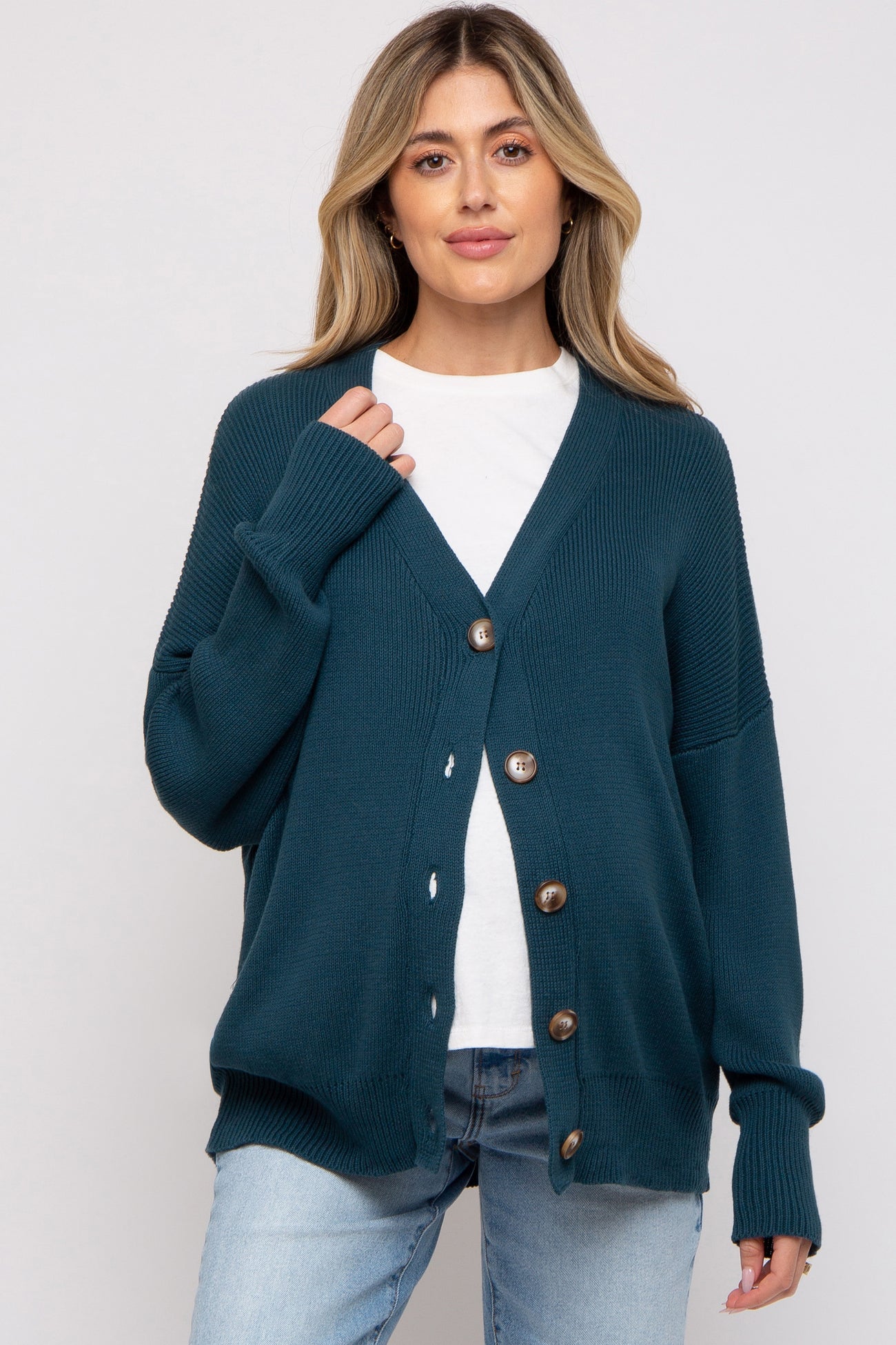 woman wearing a dark teal cardigan with buttons over a white t-shirt and light blue jeans, no visible baby bump