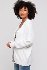 woman wearing a white chunky knit cardigan with buttons, styled over a gray top and blue jeans