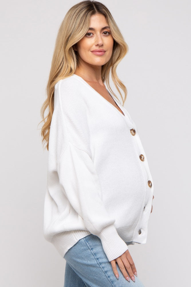 woman wearing a white oversized knit maternity cardigan with button details and a visible baby bump