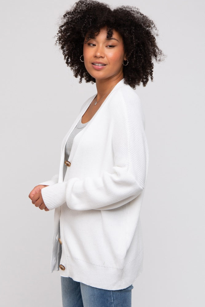 woman wearing a white chunky knit cardigan with buttons, styled over a gray top and blue jeans