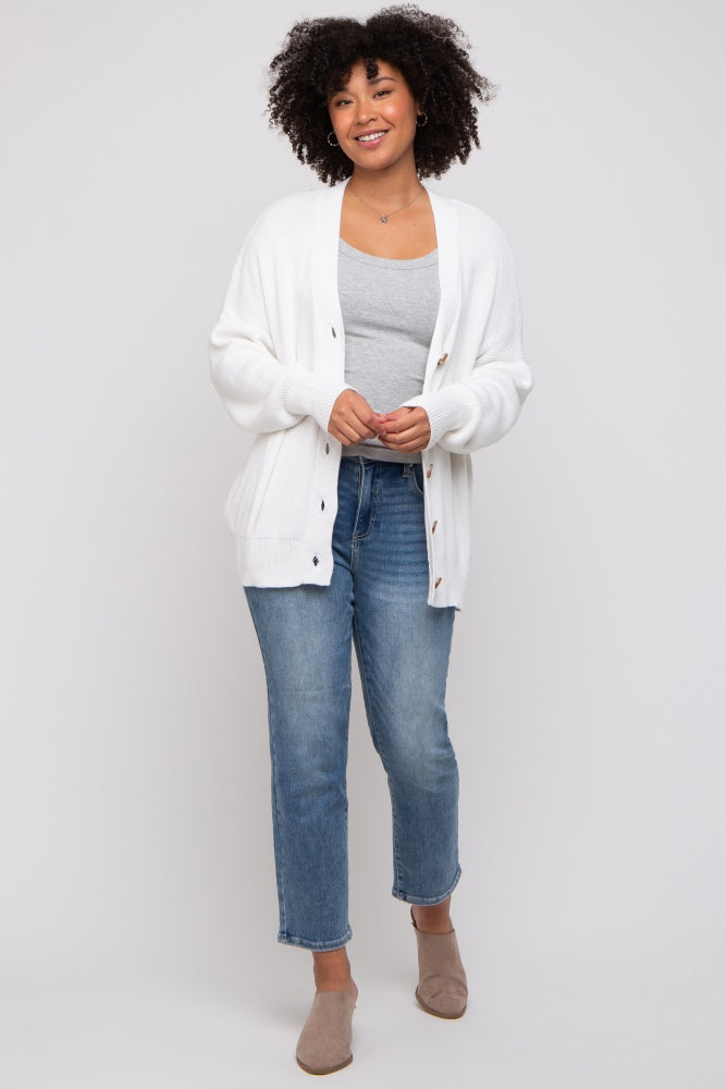woman wearing a white knit cardigan over a gray tank top, paired with light blue jeans and beige slip-on shoes