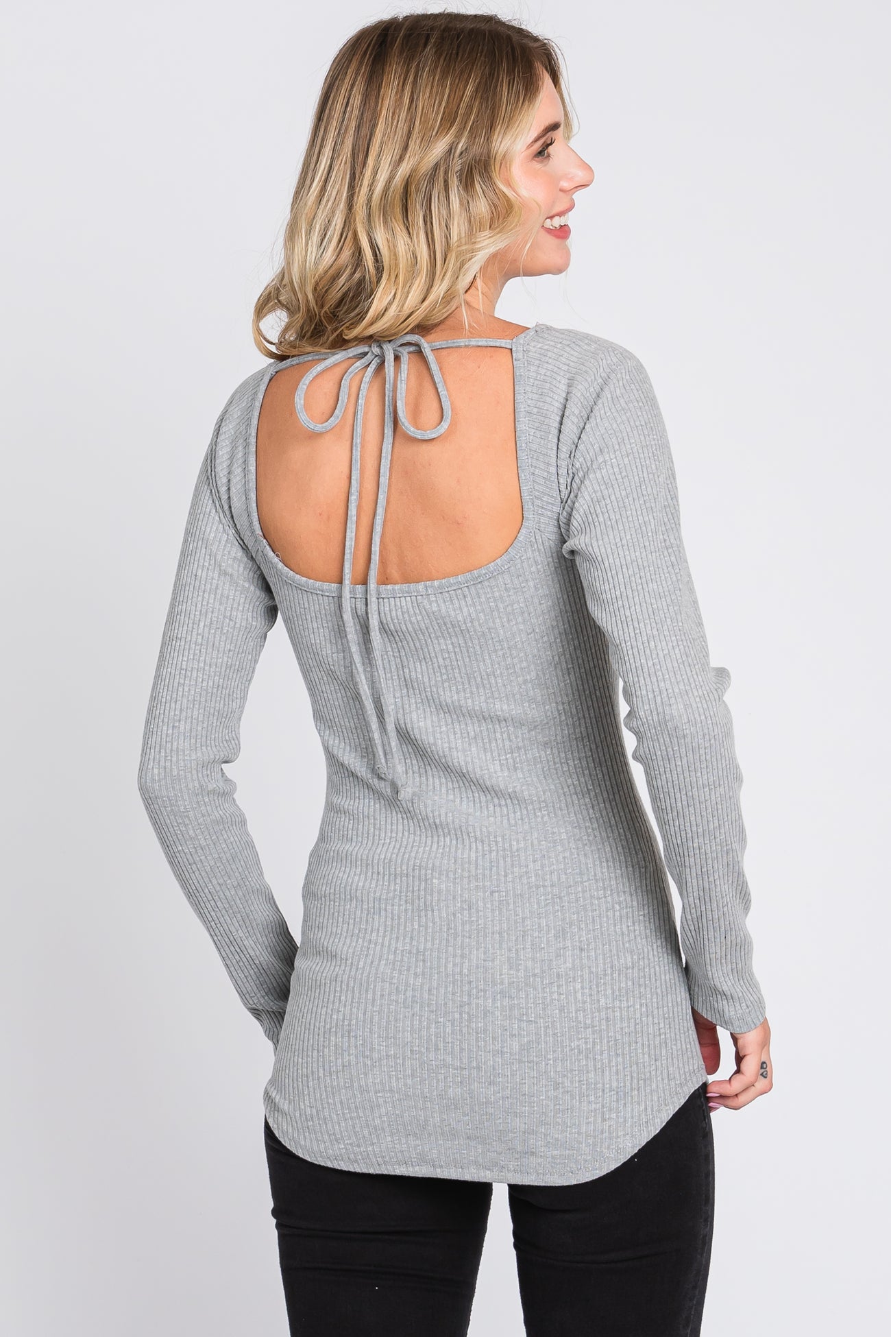 woman wearing a light gray ribbed long sleeve top with a tie-back detail and a curved hemline