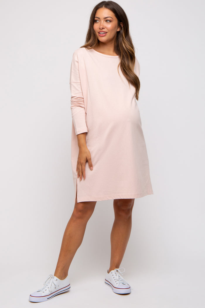 woman wearing a light pink long sleeve maternity dress with a side slit and a visible baby bump