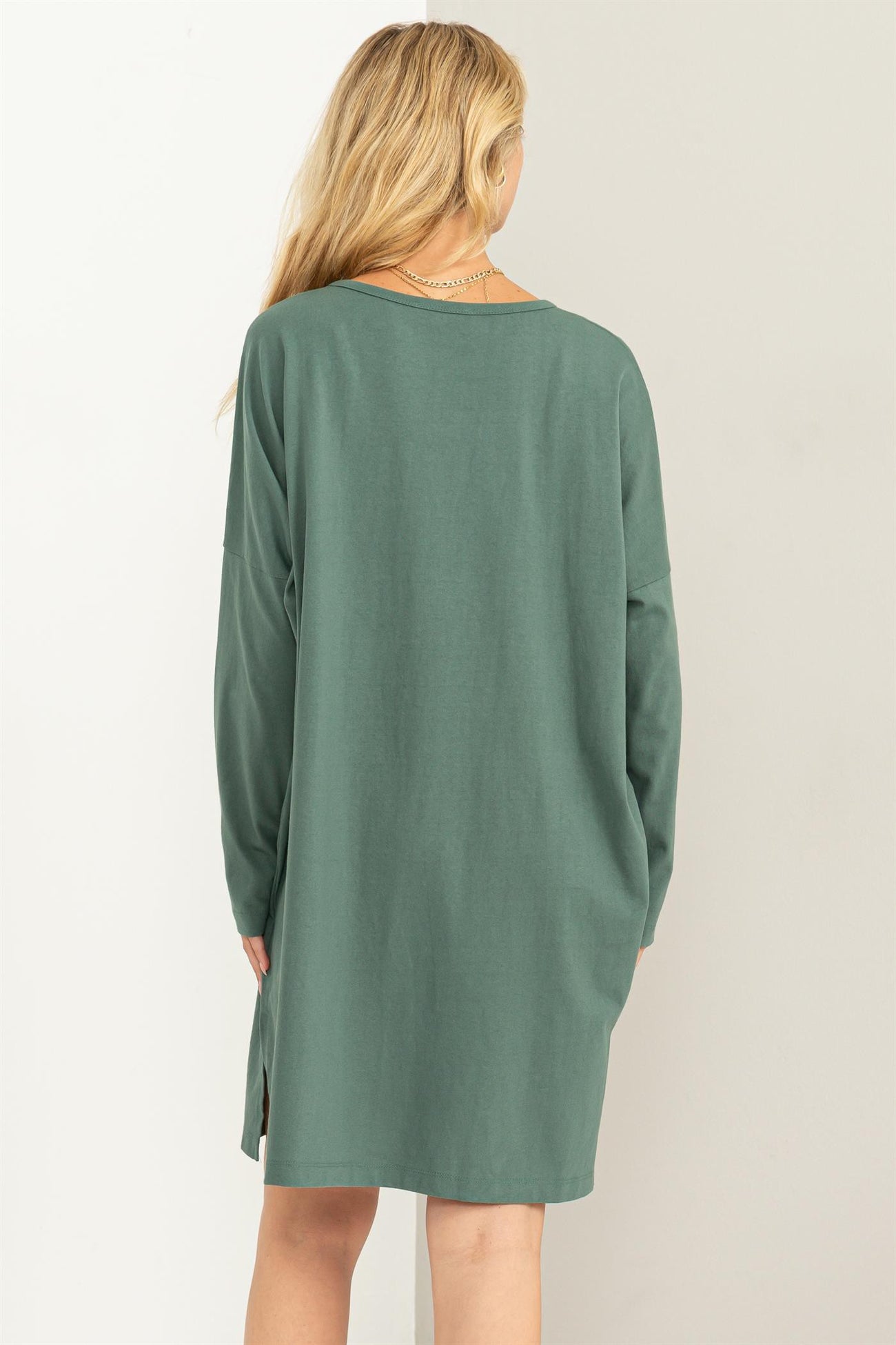 woman wearing a green long sleeve oversized dress with side slits, viewed from the back