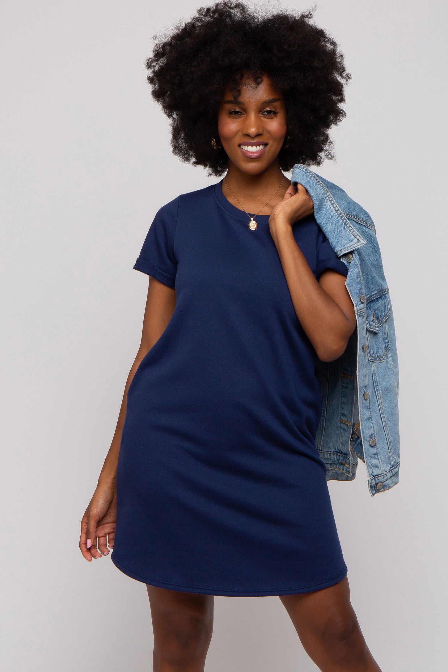 woman wearing a navy blue short sleeve t-shirt dress and holding a denim jacket over her shoulder