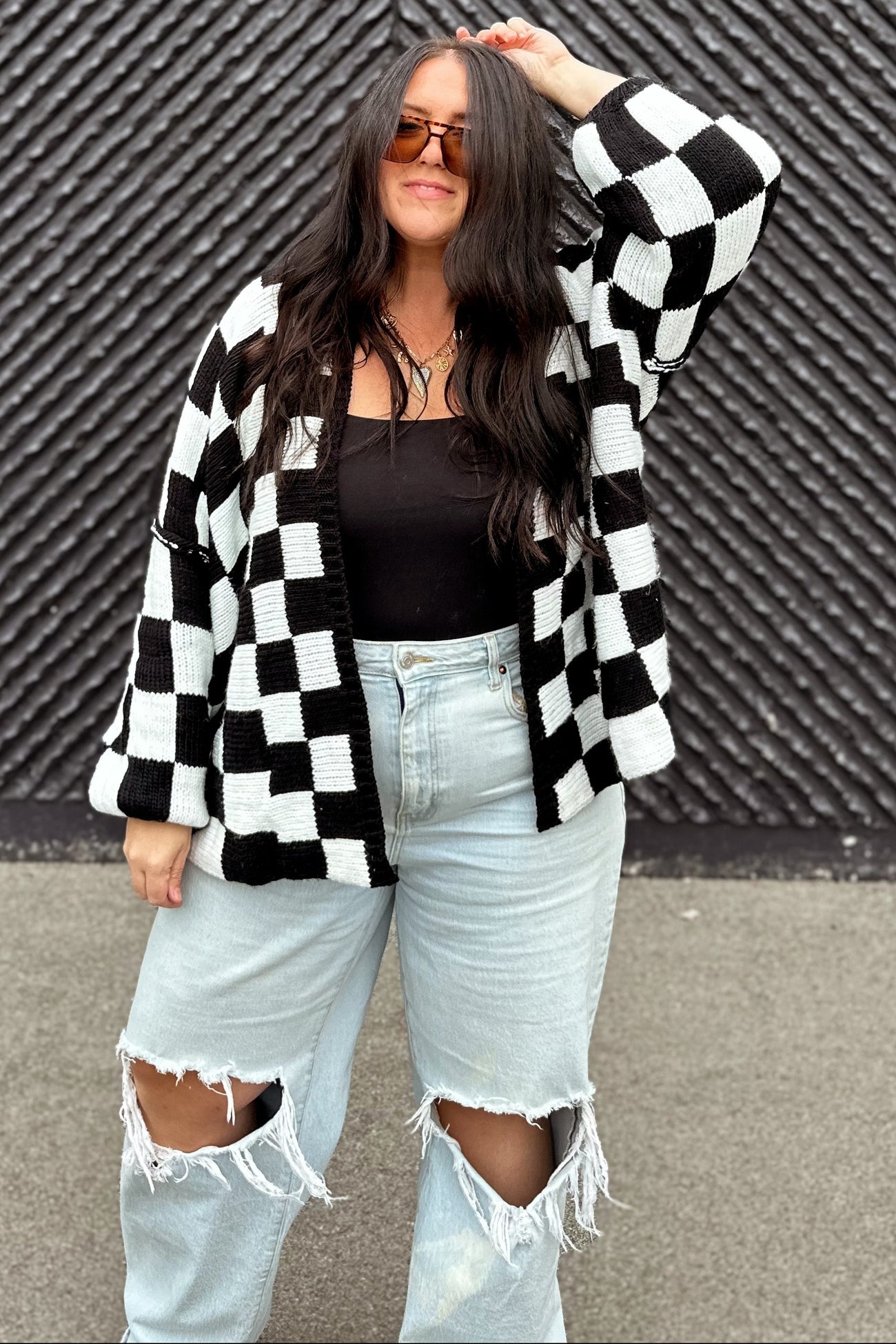 woman wearing a black and white checkered cardigan over a black top and distressed light blue jeans