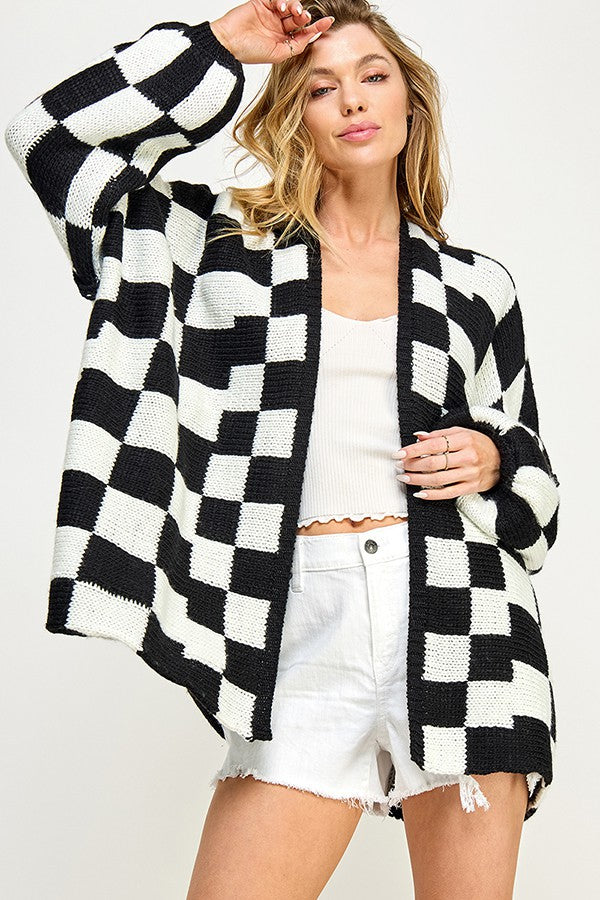 woman wearing a black and white checkered cardigan over a white crop top and white shorts