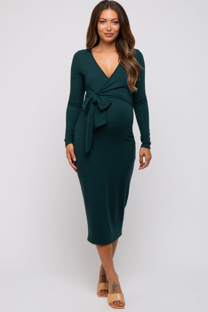 woman wearing a dark green long sleeve maternity dress with a tie detail at the waist and a visible baby bump