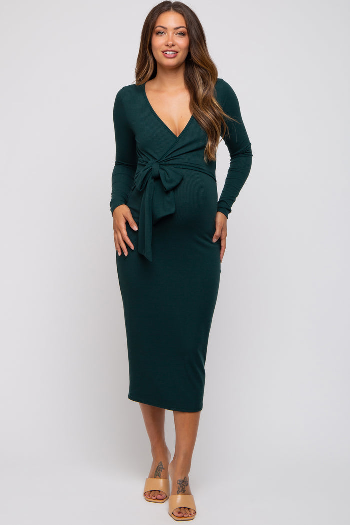 woman wearing a dark green long sleeve maternity dress with a tie waist and a deep v-neck, showing her baby bump