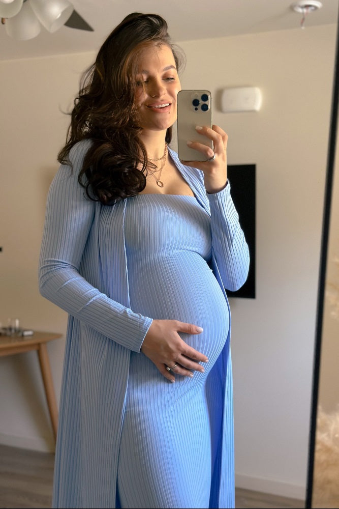 woman wearing a light blue maternity dress with a long cardigan and holding her baby bump