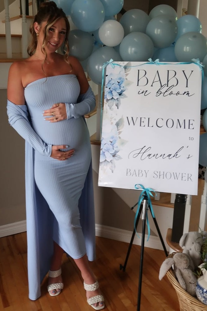 woman wearing a light blue ribbed off-shoulder maternity dress with a side slit and holding her baby bump